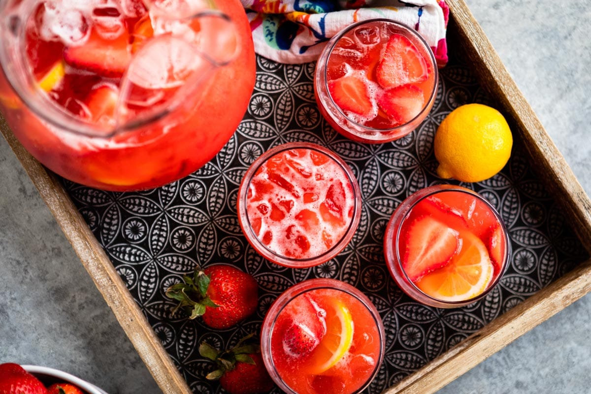 strawberry lemonade in a glass jar on a tray with fresh fruit ingredients.