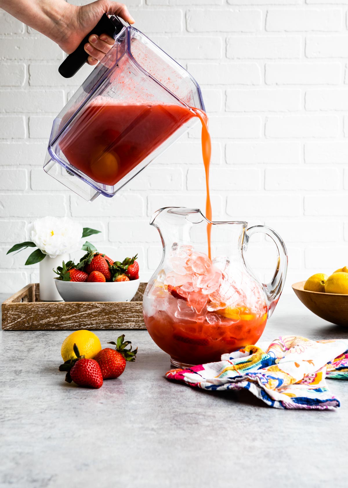 pouring homemade strawberry lemonade from the blender to a glass pitcher full of ice.