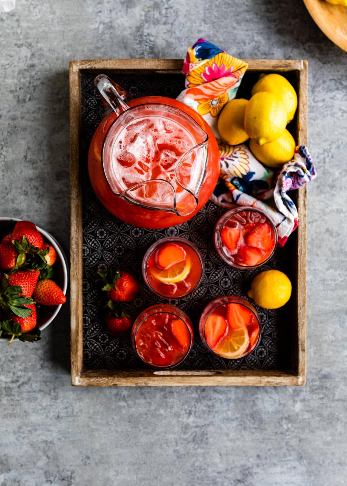 4 glasses of red beverage with fresh strawberries and lemons.