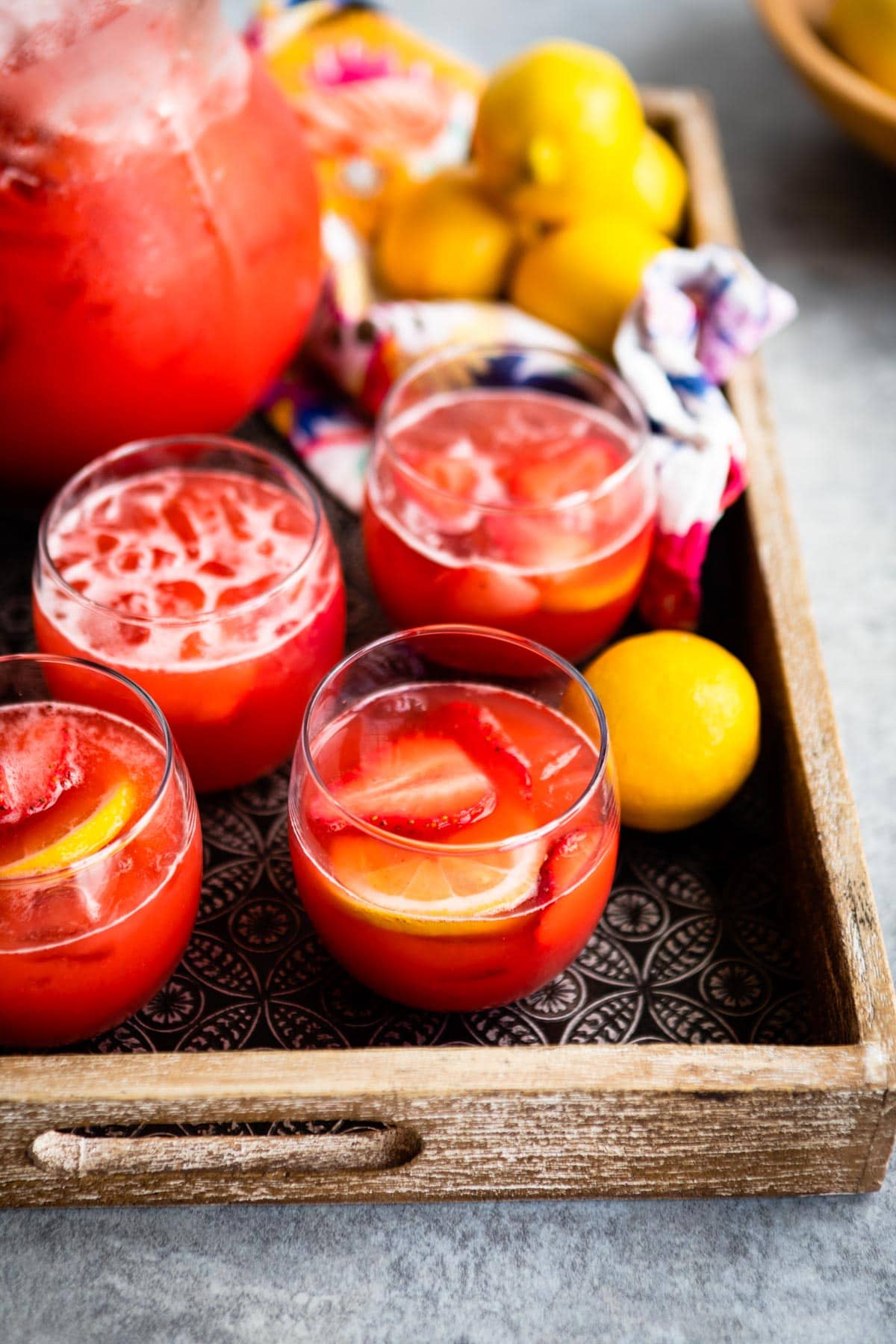 homemade strawberry lemonade in glasses on a tray with whole lemons.