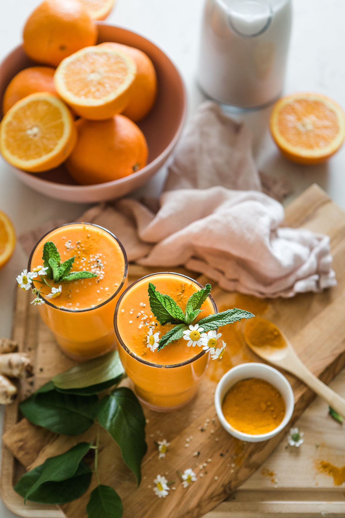 Two glasses of bright orange turmeric smoothie garnished with fresh mint and small white flowers