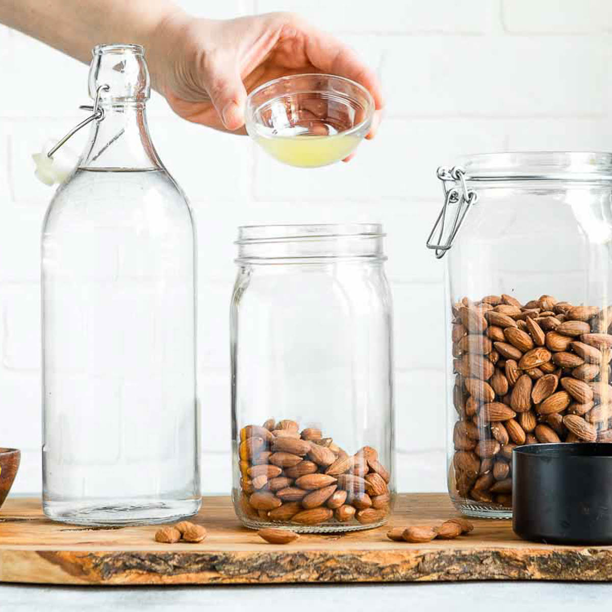 A hand pouring lemon juice into a jar of almonds.