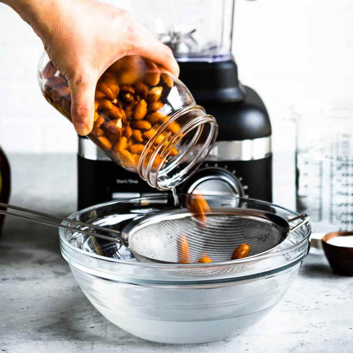 A person pouring almonds into a strainer.