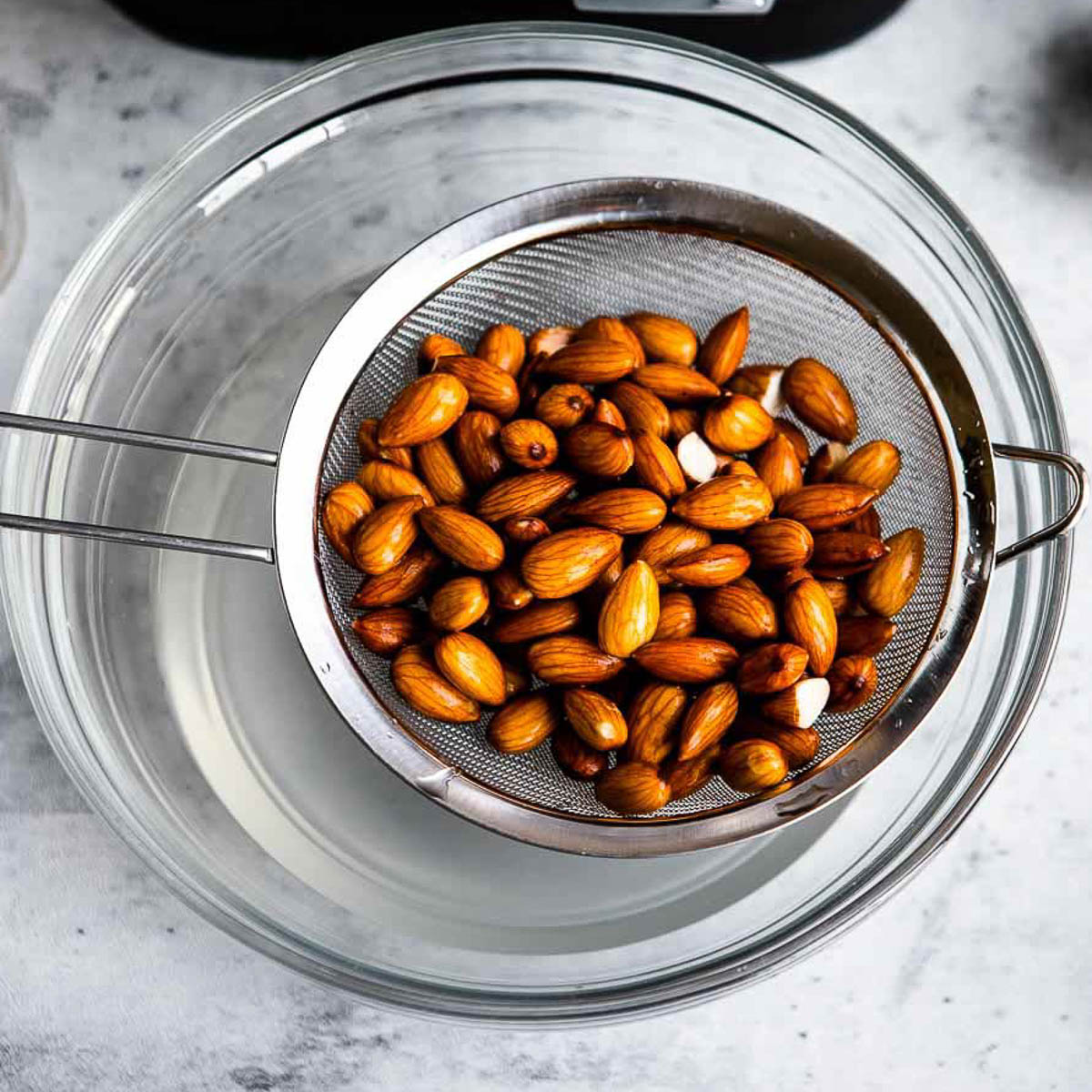 Almonds being rinsed in a strainer over a bowl of water.