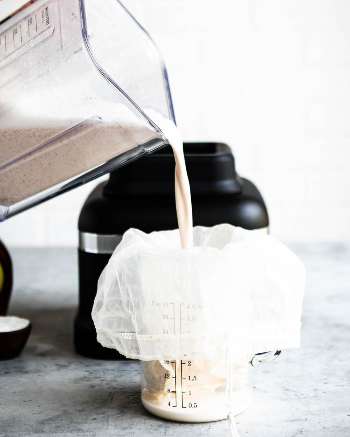 Almond milk being poured from a blender into a nut milk bag.