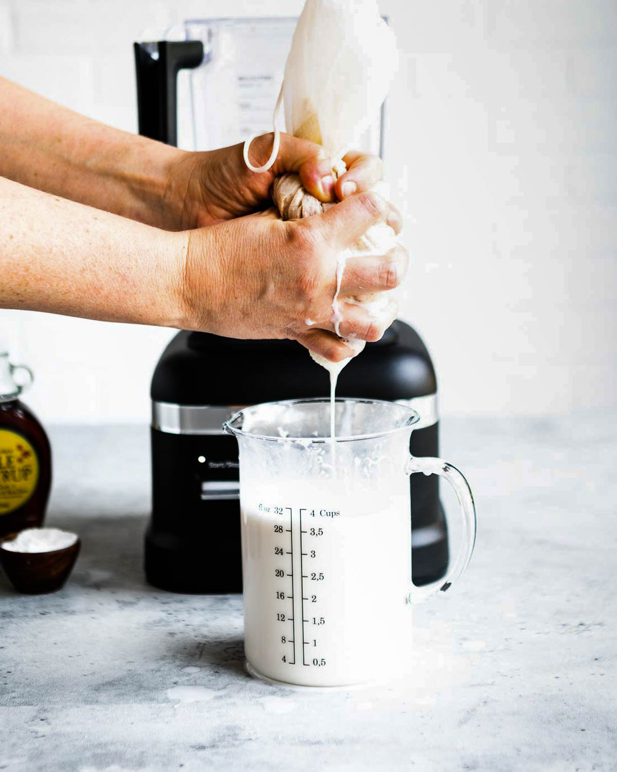 A person squeezing a cheesecloth into a measuring cup.