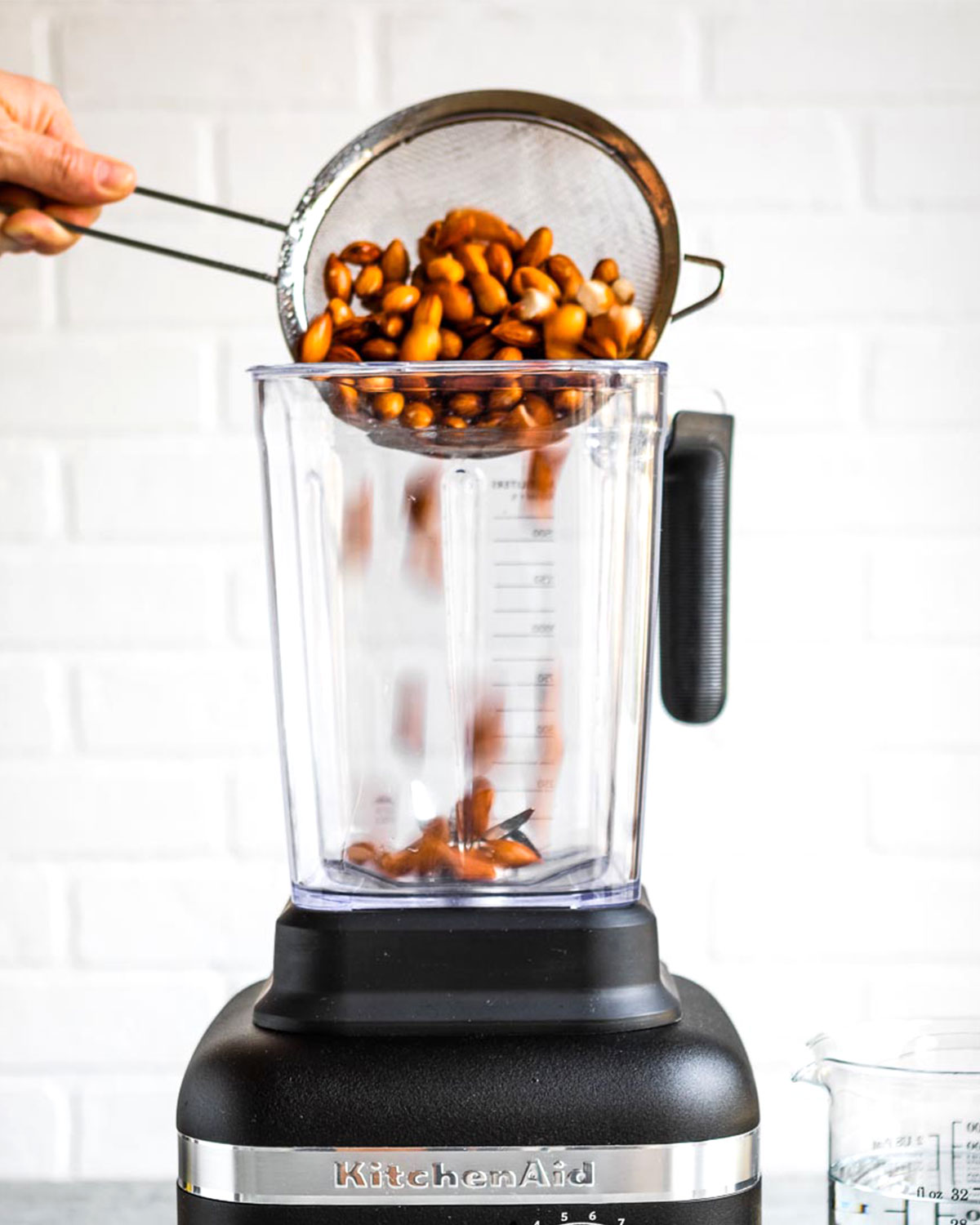 Almonds being poured into a blender from a strainer.