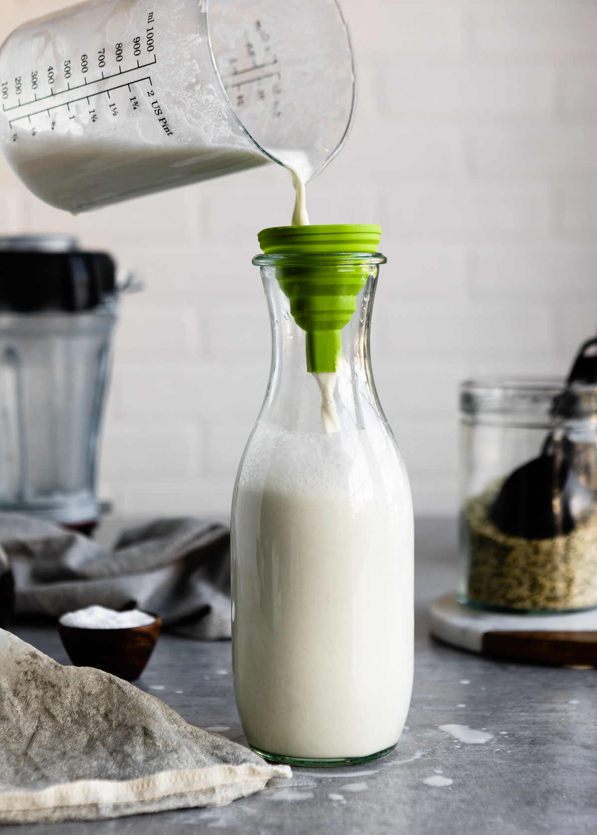 Pouring homemade hemp milk through a funnel into a glass bottle.