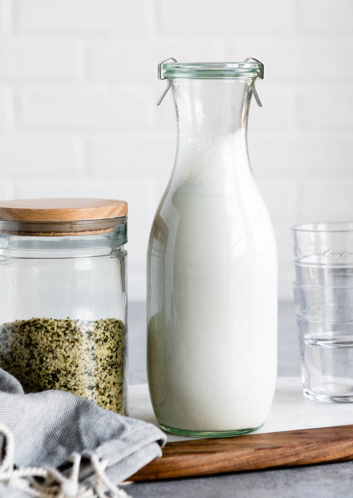 glass jar of hemp milk next to a jar of hemp hearts and short glasses.