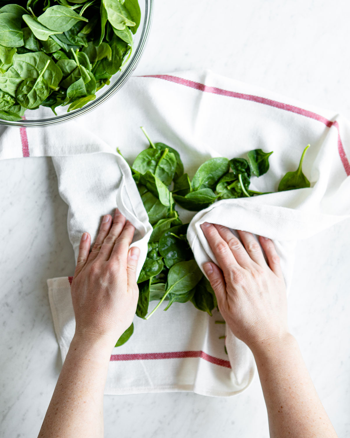 Hands padding dry spinach with a clean towel.