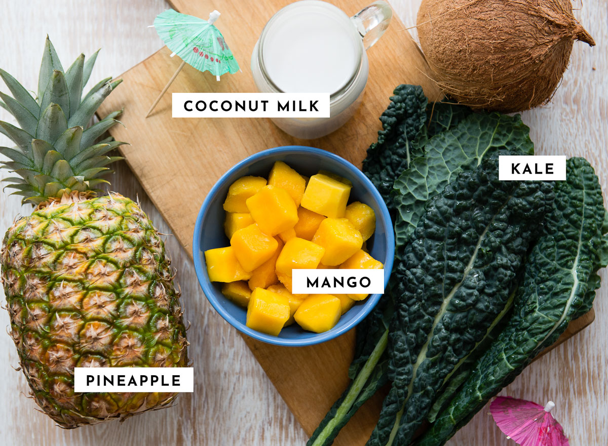 Labeled ingredients for a kale mango smoothie, including mango, kale, pineapple, and coconut milk.