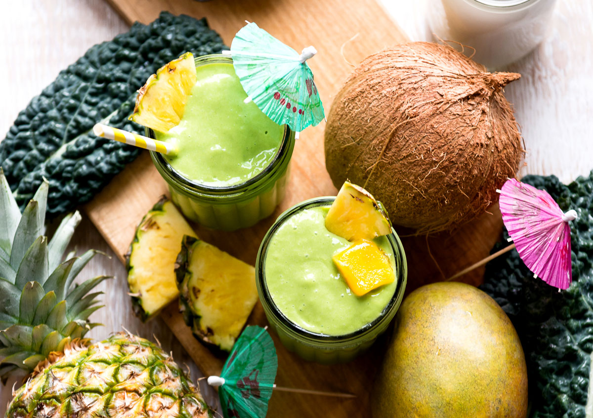 Two kale mango smoothies in glasses with tropical umbrellas.