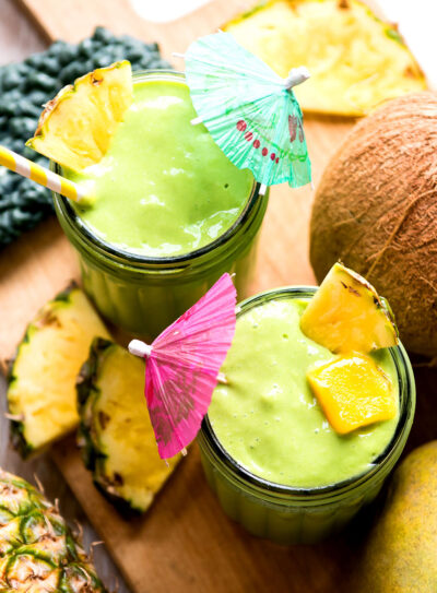 Two kale mango smoothies in glasses with tropical umbrellas.