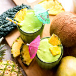 Two kale mango smoothies in glasses with tropical umbrellas.