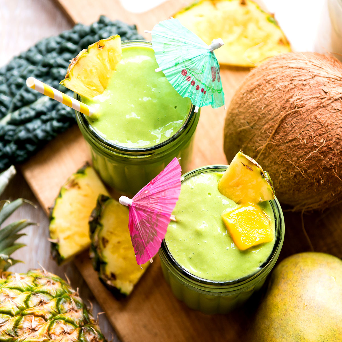 Two kale mango smoothies in glasses with tropical umbrellas.