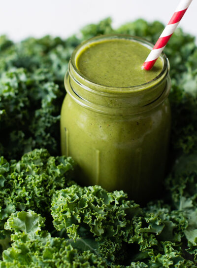 A green smoothie in a Mason jar, nestled among fresh kale leaves