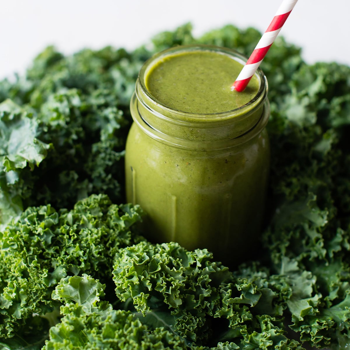 A green smoothie in a Mason jar, nestled among fresh kale leaves