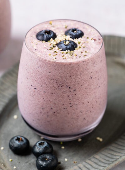 A glass filled with a light purple low-calorie protein shake, garnished with fresh blueberries