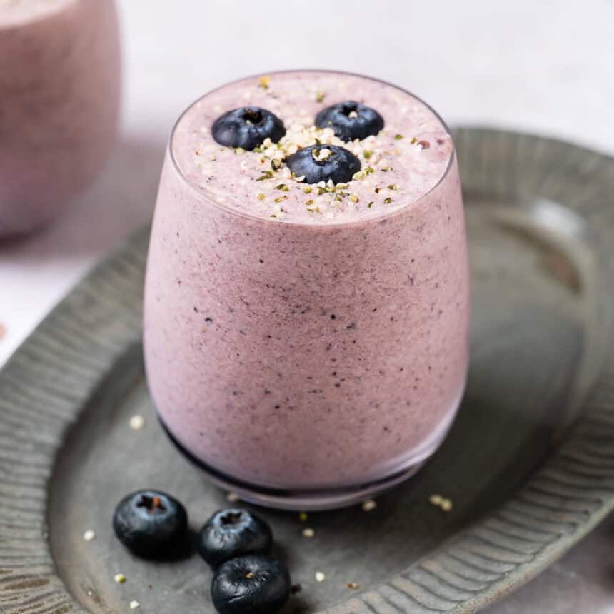 A glass filled with a light purple low-calorie protein shake, garnished with fresh blueberries