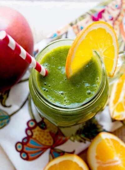 green smoothie in a glass jar with a paper striped straw and an orange slice on the rim.