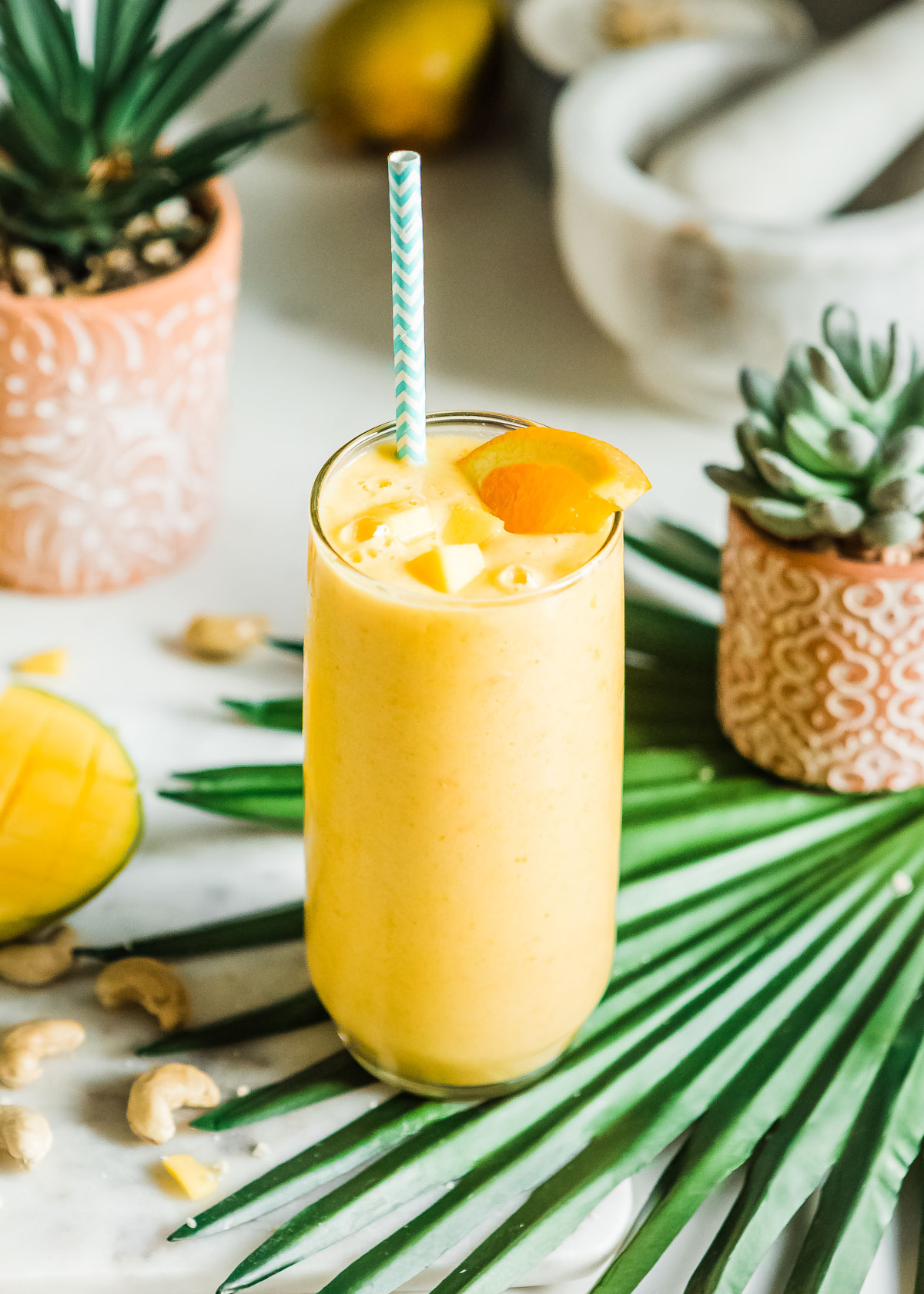 Creamy mango smoothie garnished with an orange slice, mango chunks, and a paper straw.