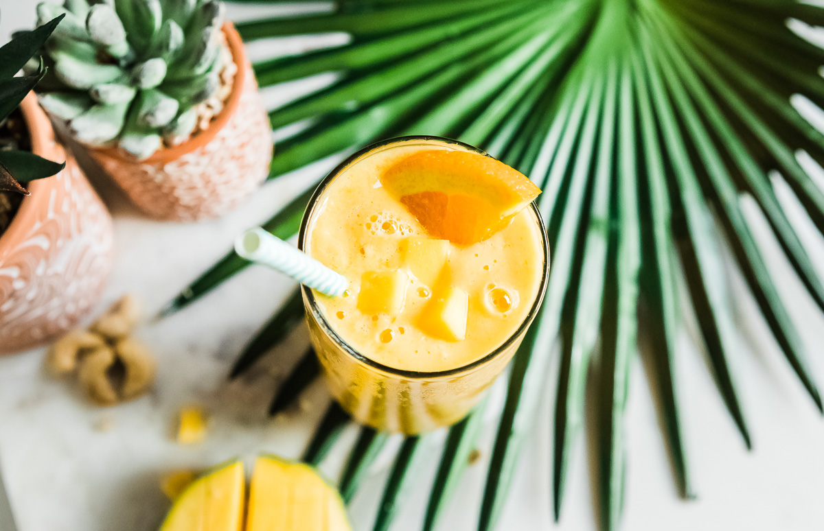 Top-down view of a mango smoothie garnished with an orange slice, mango chunks, and a paper straw.