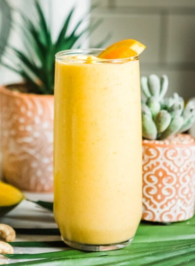 Mango smoothie in a tall glass, garnished with an orange wedge.