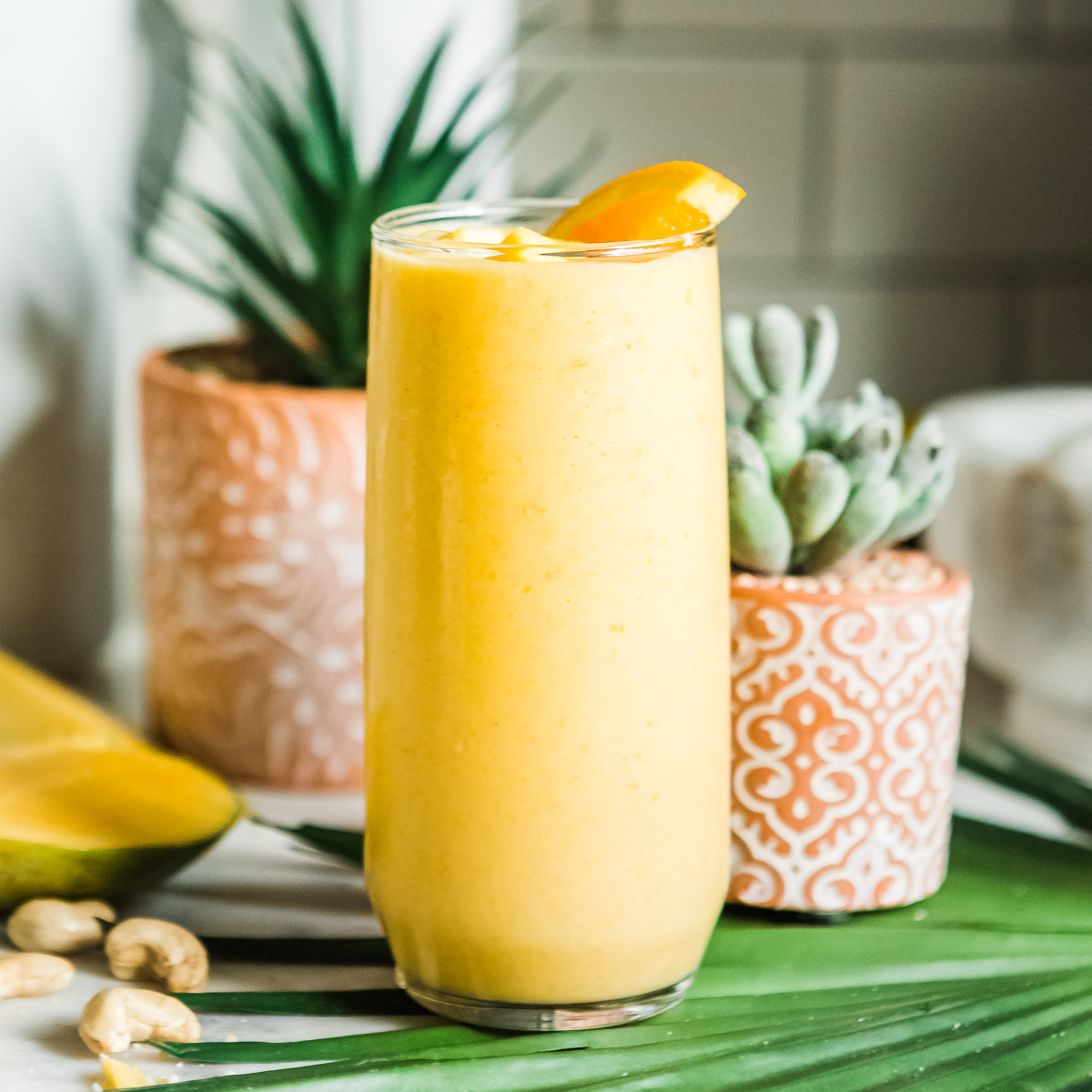 Mango smoothie in a tall glass, garnished with an orange wedge.
