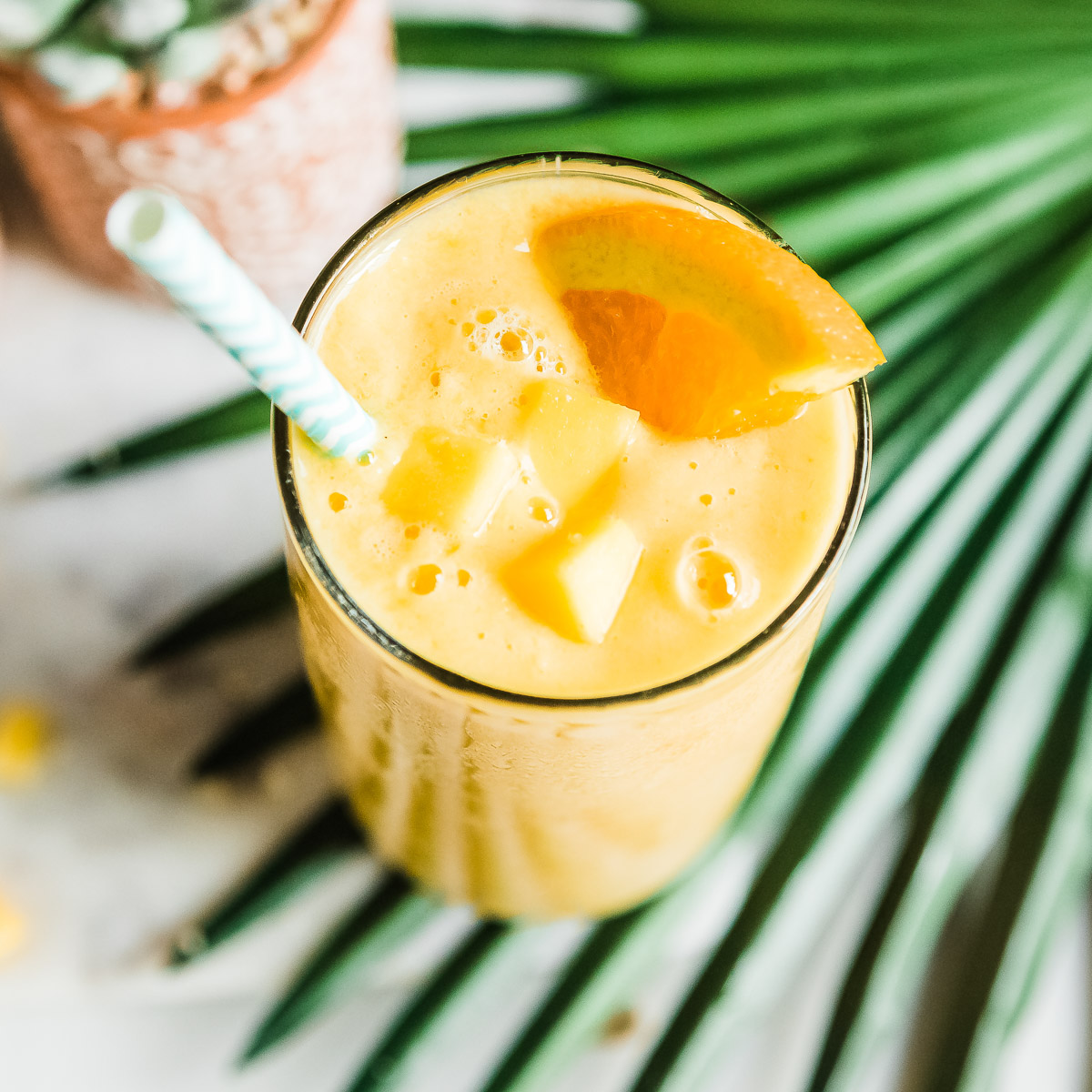 Top-down view of a mango smoothie garnished with an orange slice, mango chunks, and a paper straw.