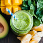 Overhead view of a mango spinach smoothie in a glass Mason jar surrounded by fresh ingredients.