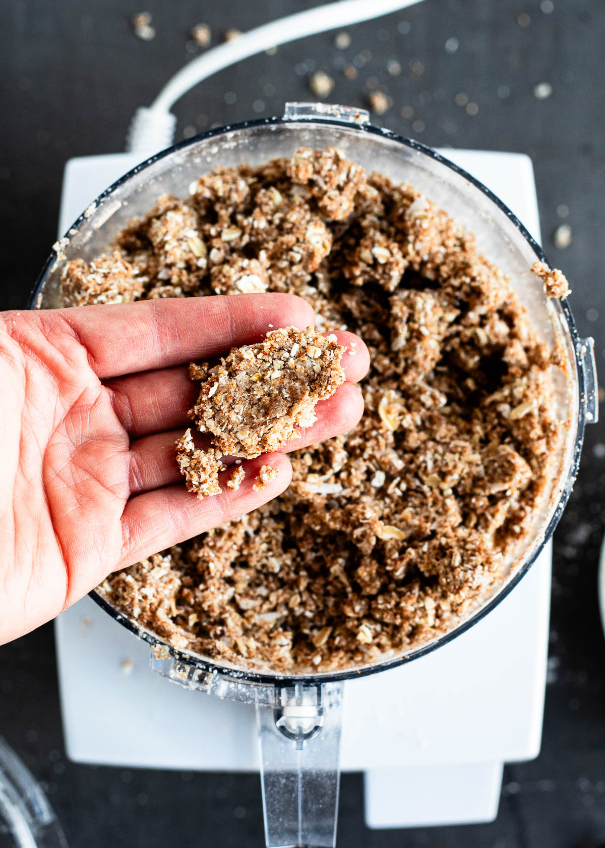 A person holding crumbly mixture of flour, flaxseeds, coconut oil and coconut sugar