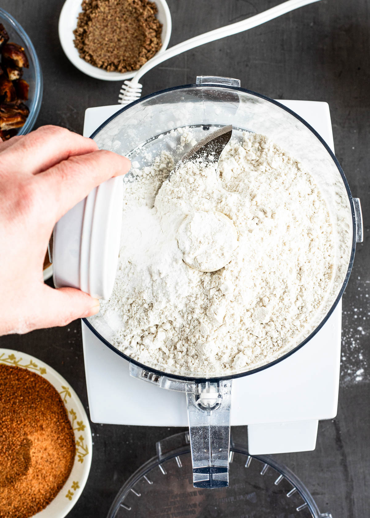 A person adding dried ingredients in a food processor