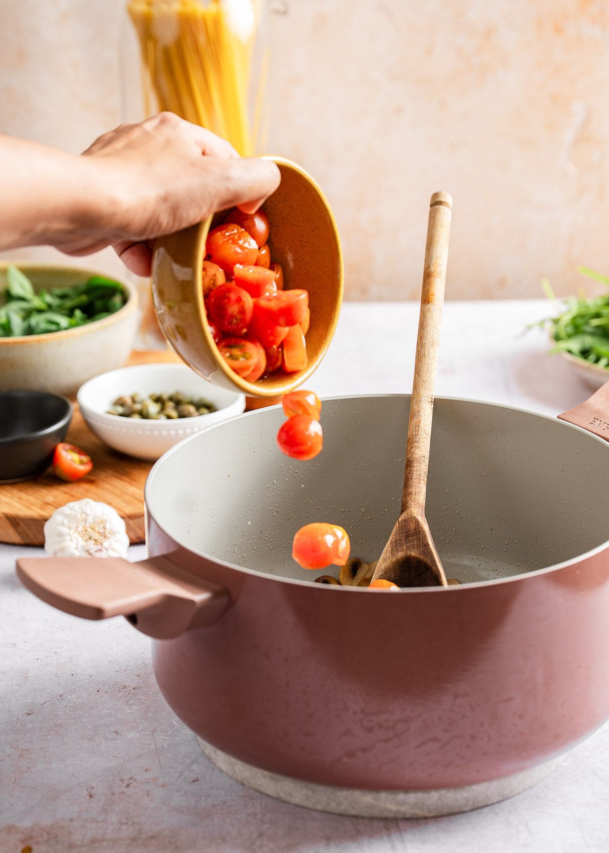 A person adding cherry tomatoes in the pot for pasta
