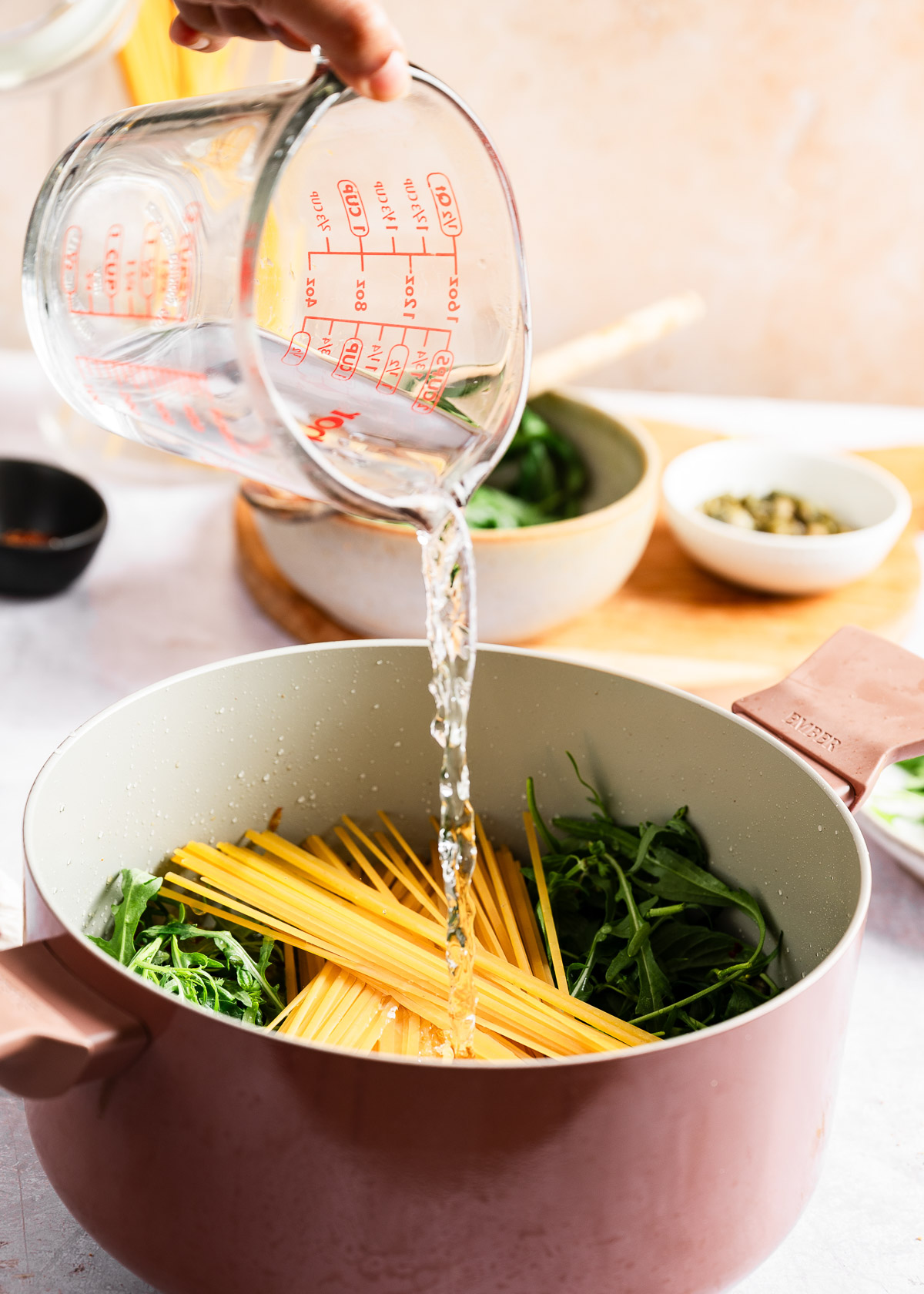 A person pouring reserved pasta water over ingredients in a pot