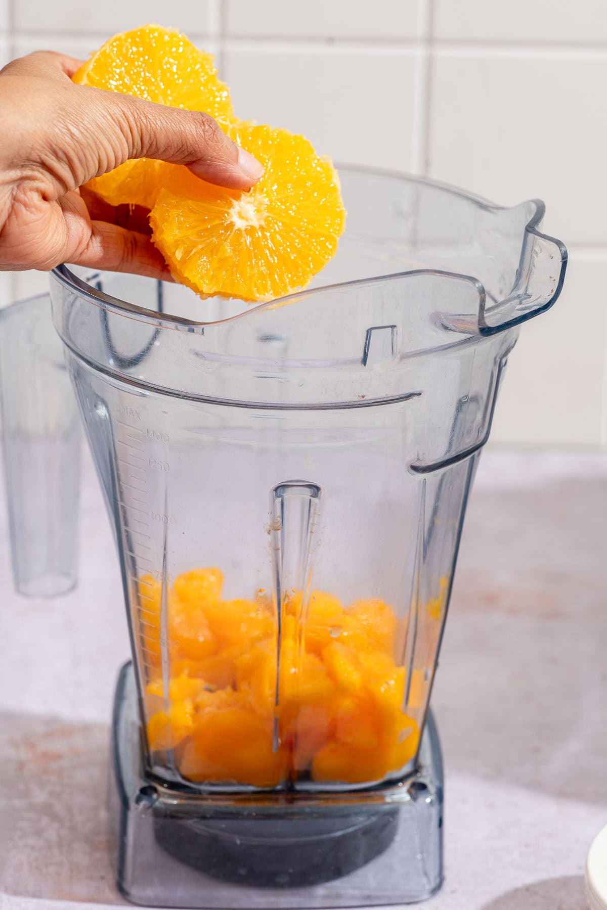 Peeled orange slices going into a blender jar over frozen mango chunks.