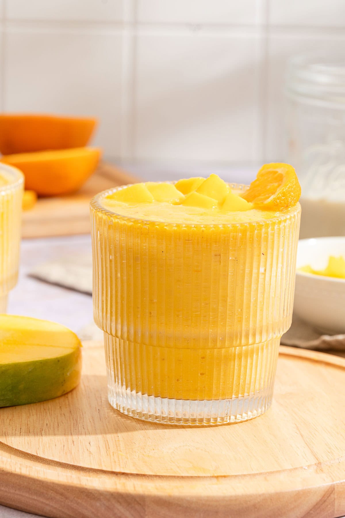 Finished ribbed glass of thick orange mango smoothie with an orange slice on the rim.