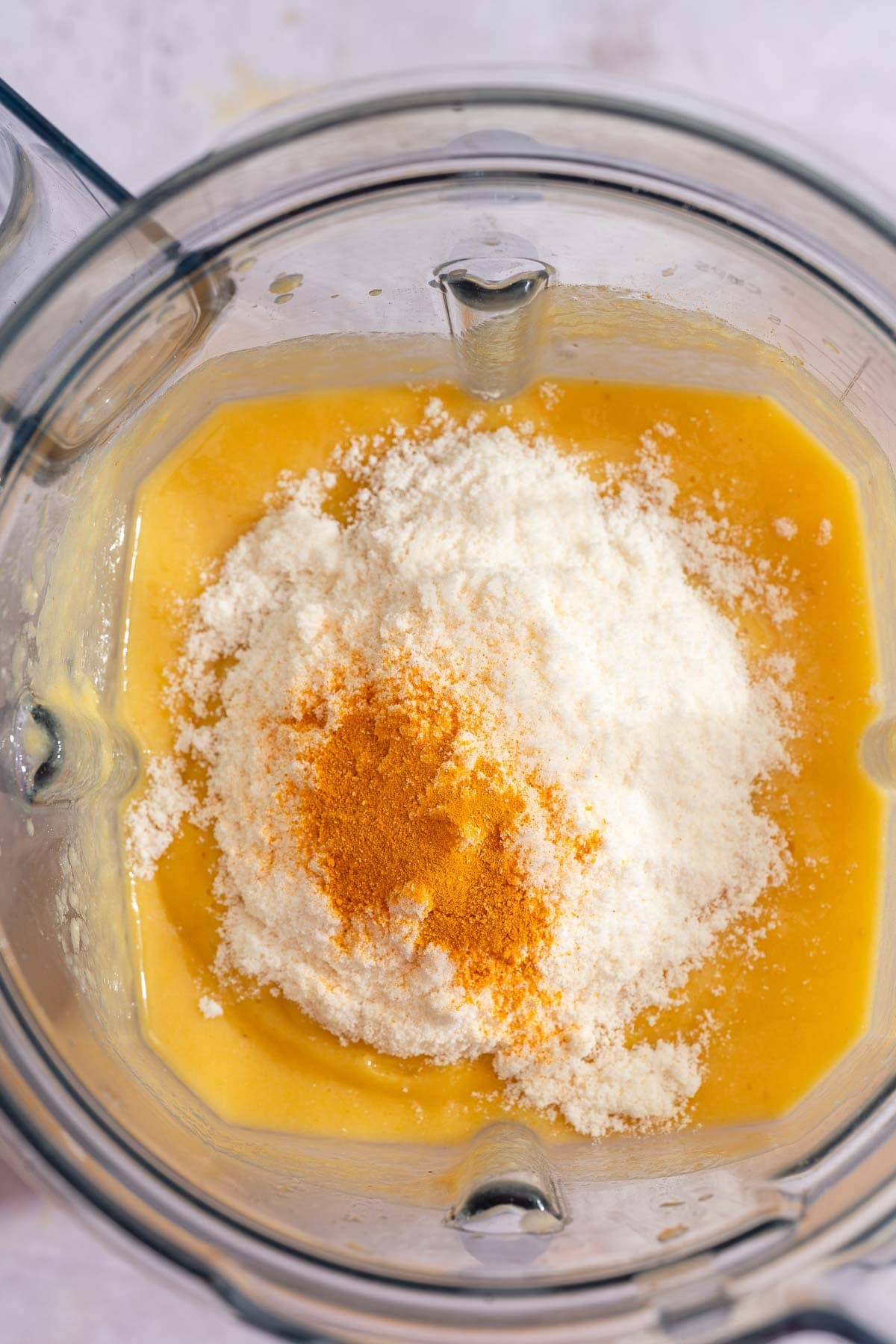 Top-down view of protein powder and turmeric sitting on the blended orange smoothie in the blender.