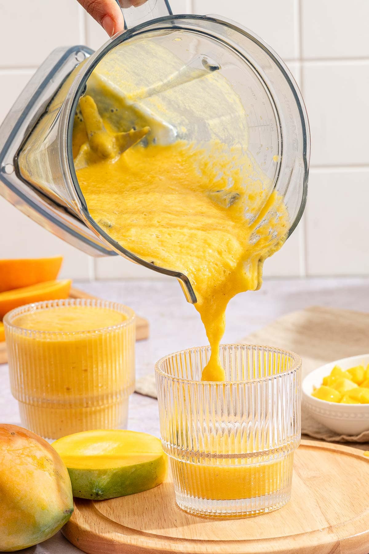Thick orange mango smoothie being poured from the blender into a ribbed glass.