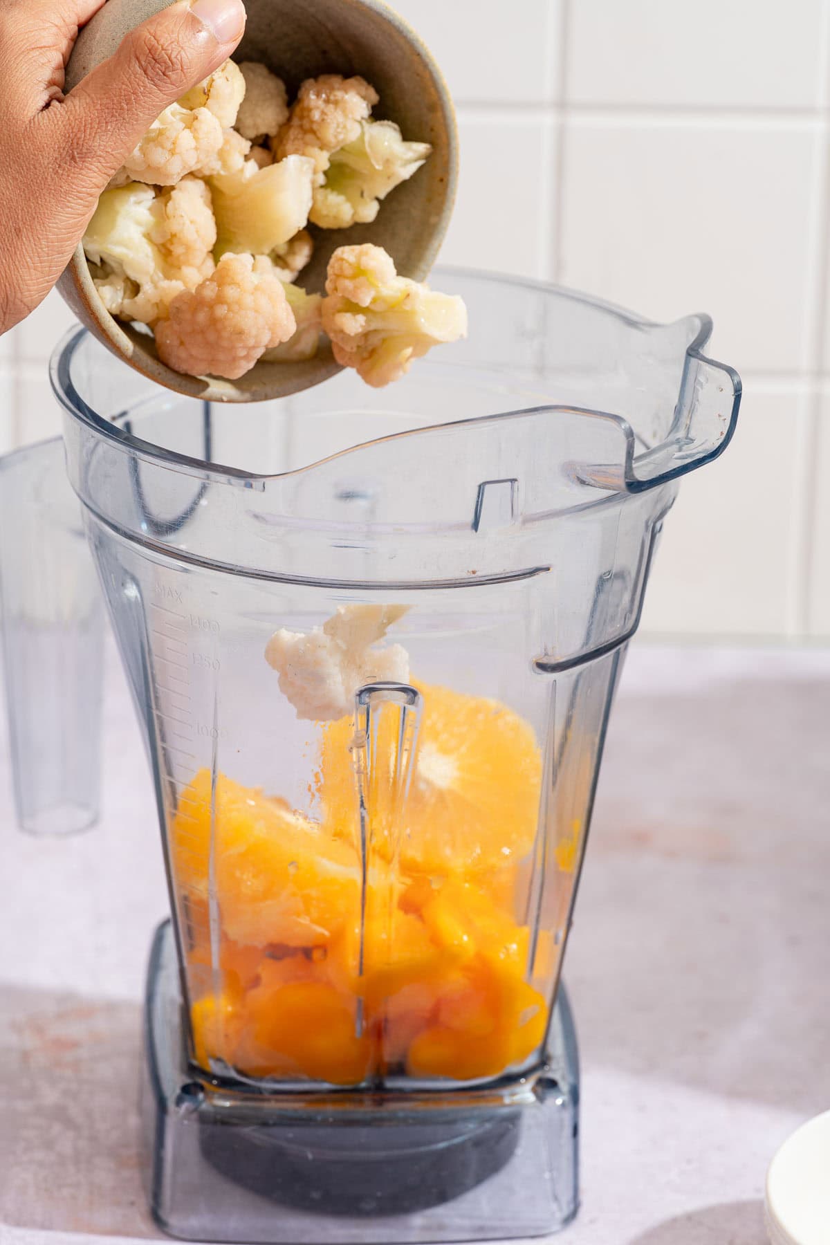 Frozen cauliflower florets being added to the blender with mango and orange.