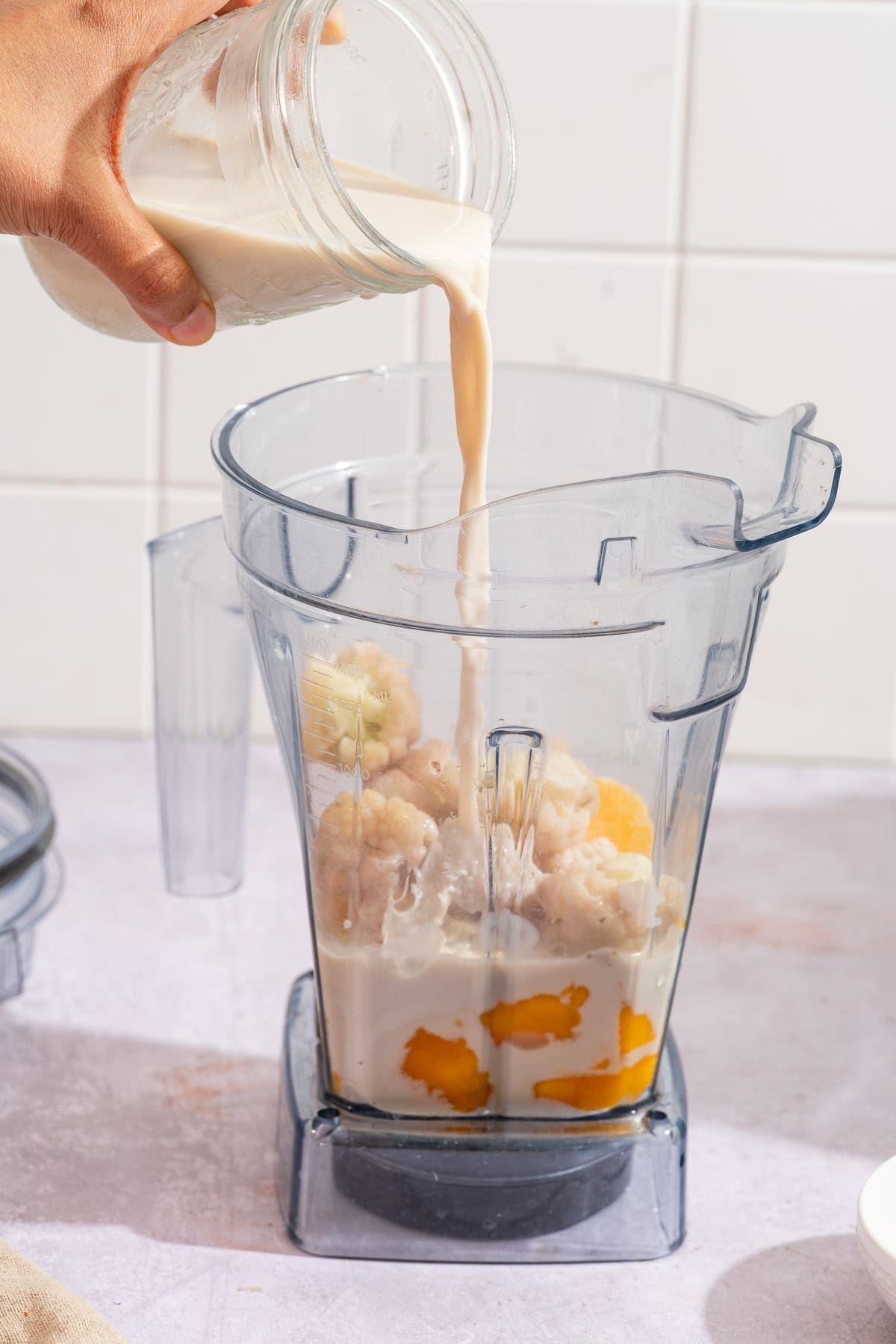 Almond milk pouring into a blender jar of cauliflower, mango and orange.