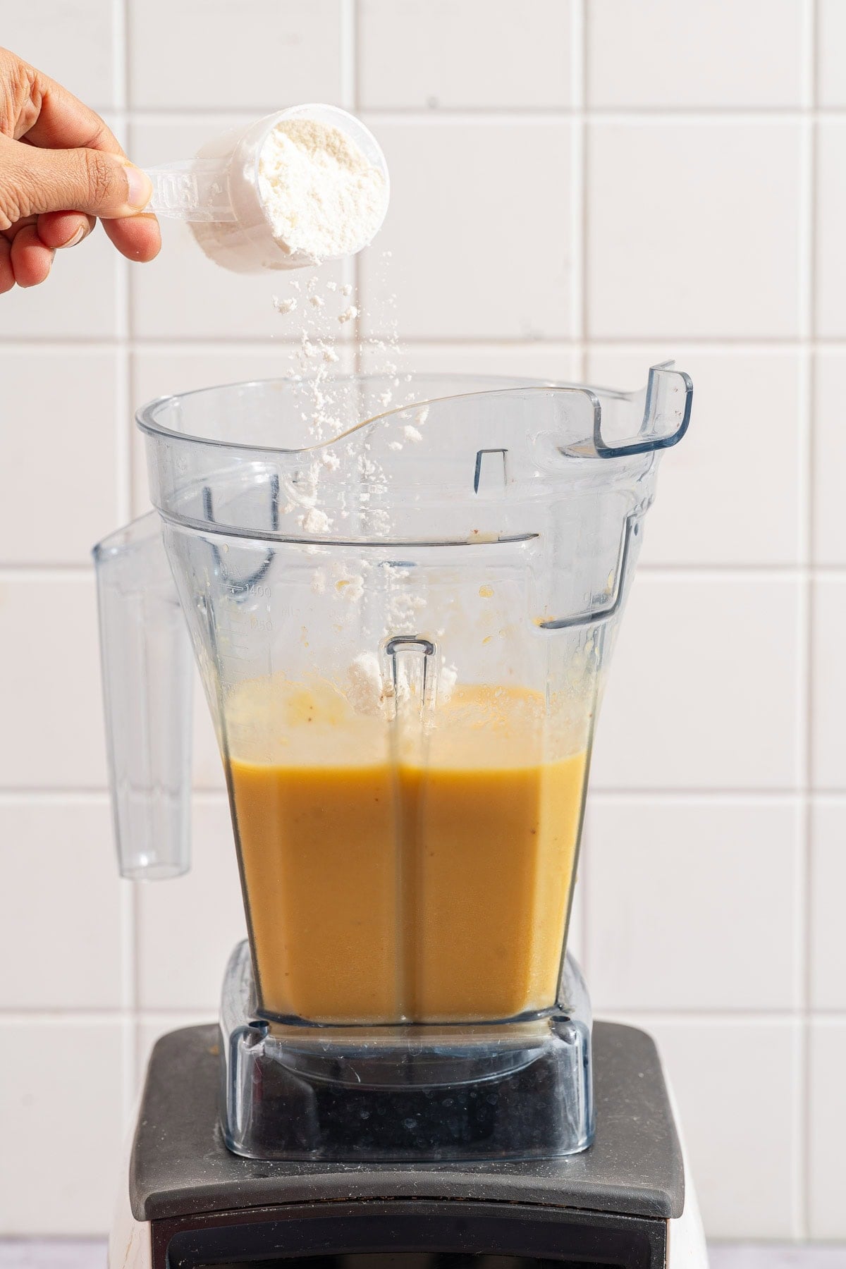 Scoop of protein powder being added to the blended orange mango smoothie base.