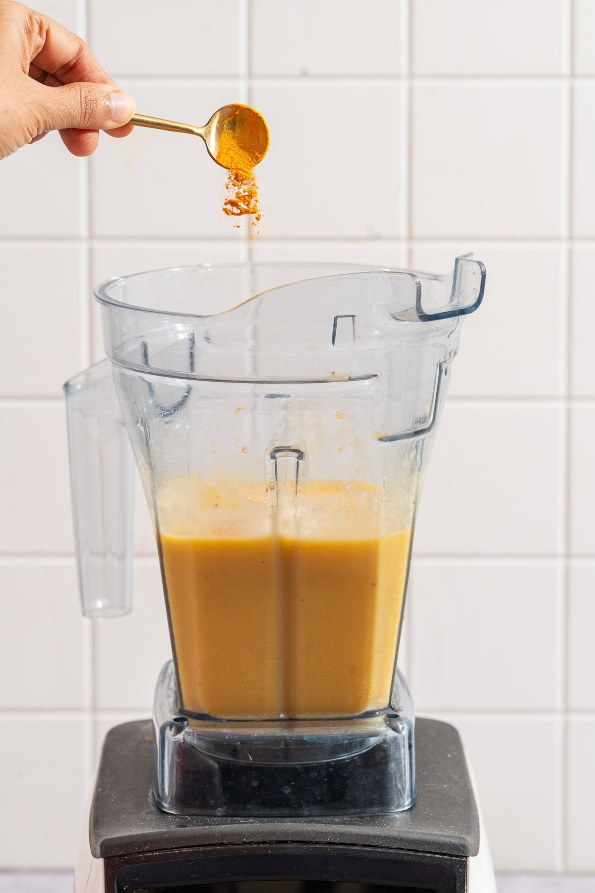 Ground turmeric added by spoon to the blender of golden smoothie base.