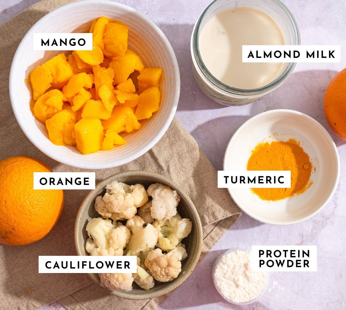 Orange mango smoothie ingredients: frozen mango, navel orange, frozen cauliflower, almond milk, turmeric and protein powder.