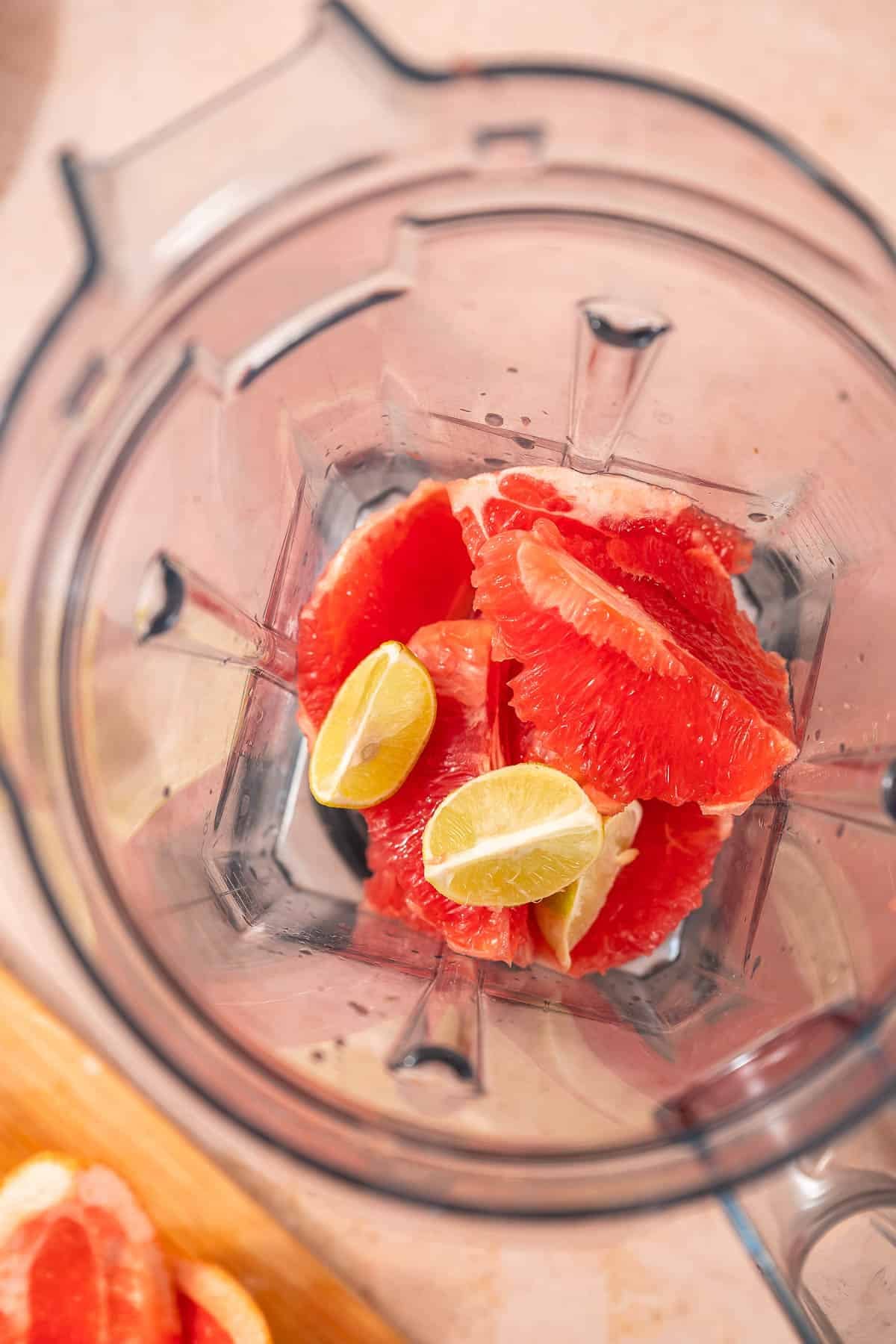 A blender containing sliced grapefruit and lime