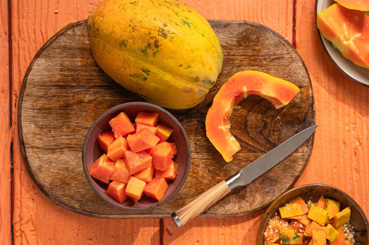 Fresh papaya and cubed papaya on a wooden cutting board with a knife