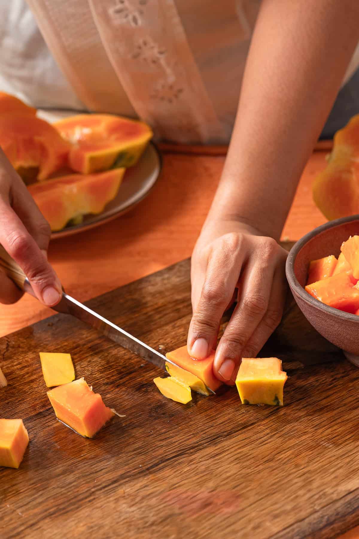 Removing papaya skin with a knife on a wooden cutting board