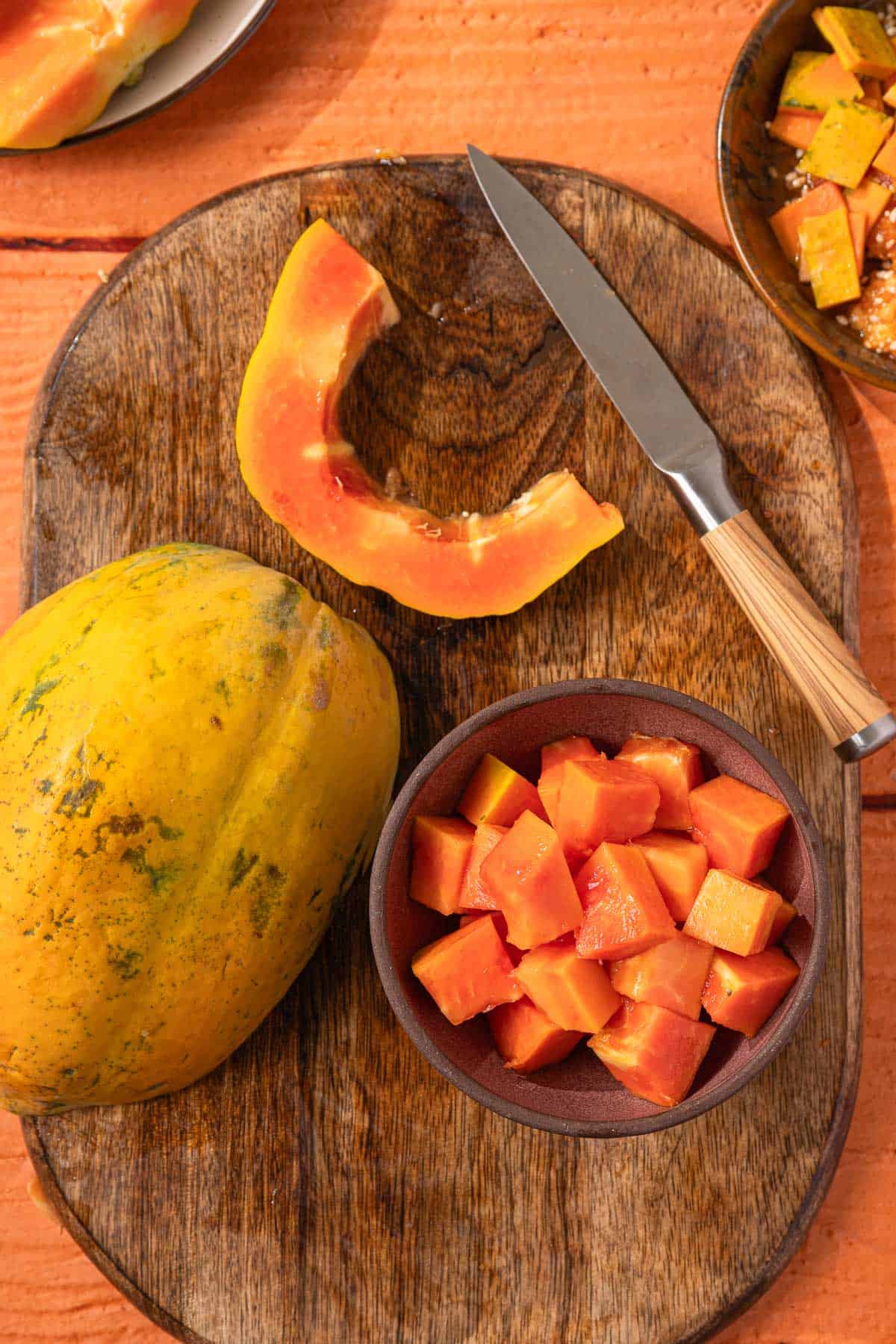 Fresh papaya slices on a wooden cutting board with a whole papaya nearby