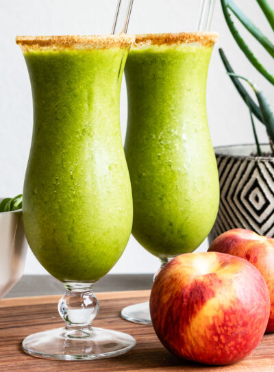 Two green smoothies in cocktail glasses, complete with glass straws and a rim of coconut sugar.