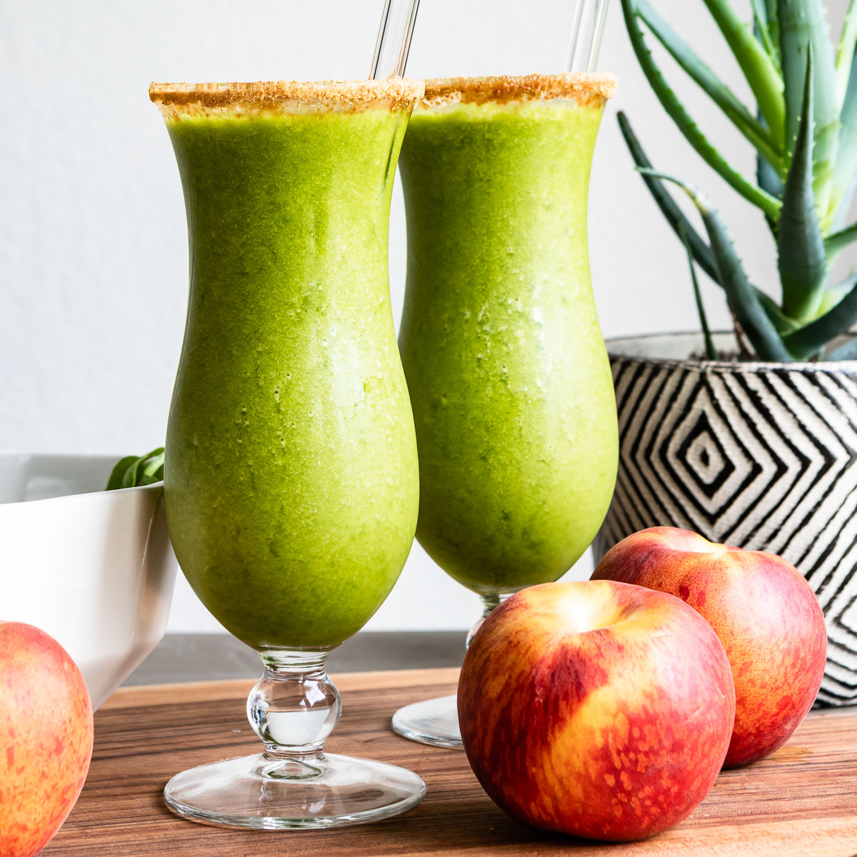 Two green smoothies in cocktail glasses, complete with glass straws and a rim of coconut sugar.