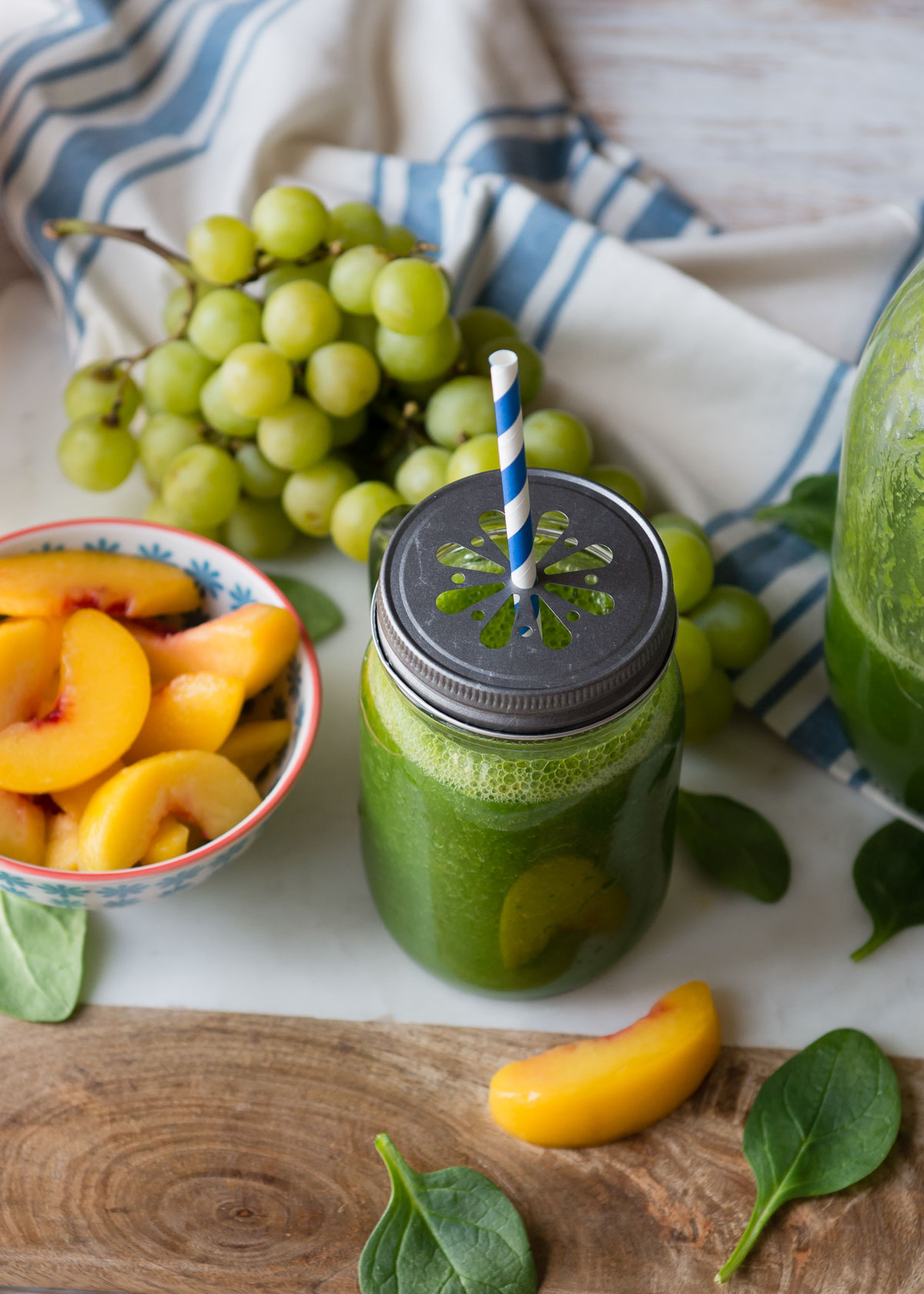green smoothie in a glass jar with a daisy cut lid and a paper straw.